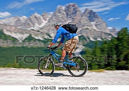 Stock Photo - Man mountain biking from Tonde De Faloria to Rio Gere with Cima De Meso Cristallo in the background high above the city of Cortina in northern Italy. Fotosearch