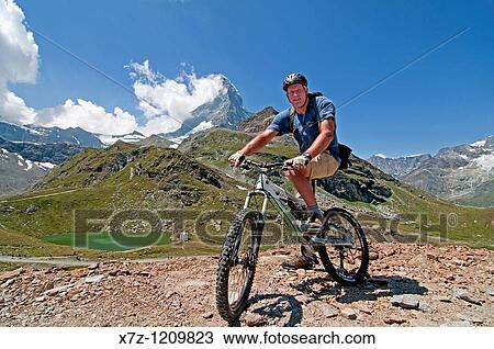 Man mountain biking in the shadow of The Matterhorn at Schwarzsee Paradise high in the Swiss Alps above the city of Zermatt in Switzerland View Large Photo Image Stock Image - Man mountain biking in the shadow of The Matterhorn at Schwarzsee Paradise high in the Swiss Alps above the city of Zermatt in Switzerland. Fotosearch