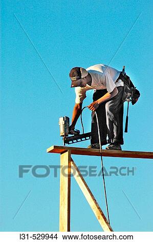 Man nailing overhead beams from above and below in dangerous positions on third floor View Large Photo Image Picture - Man nailing overhead beams from above and below in dangerous positions on third floor. Fotosearch