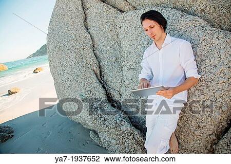 Stock Image - Man On Beach Using Ipad. Fotosearch