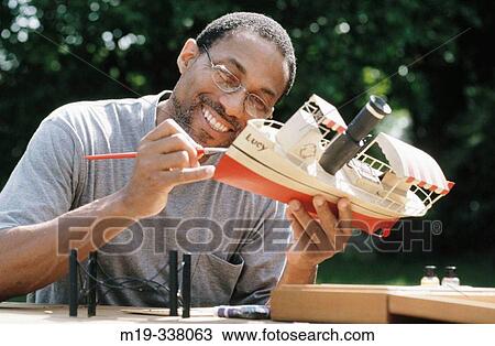 Stock Image - Man painting model boat. Fotosearch
