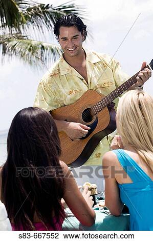 Man playing guitar for two women while they dine at the beach View Large Photo Image Stock Image - Man playing guitar for two women while they dine at the beach. Fotosearch