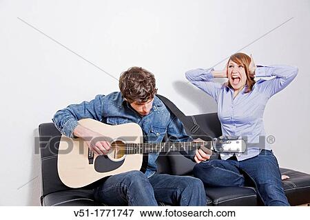 Stock Photo - Man playing guitar with his wife covering her ears. Fotosearch