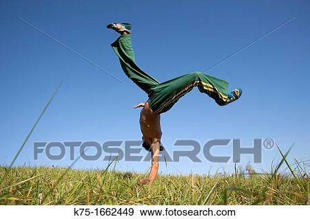 Stock Photo - Man practicing capoeira in field. Fotosearch