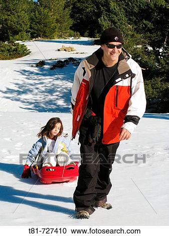 Stock Image - Man pulling a sled with his daughter on it. Fotosearch