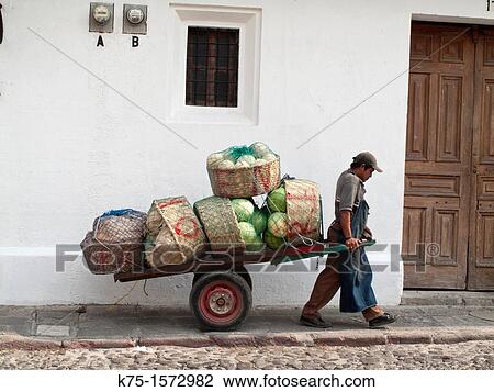 Stock Image - Man pulling delivery cart of watermelons. Fotosearch