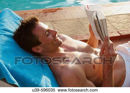 Stock Photography - Man reading a book whilst on a sunlounger by a pool in India.. Fotosearch