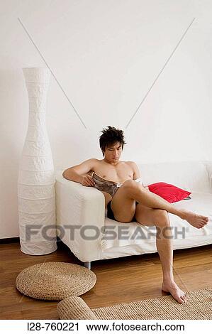 Stock Image - man reading magazine on sofa. Fotosearch