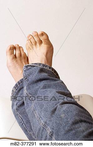 Stock Image - Man resting his feet on a white stool against a white studio background.. Fotosearch