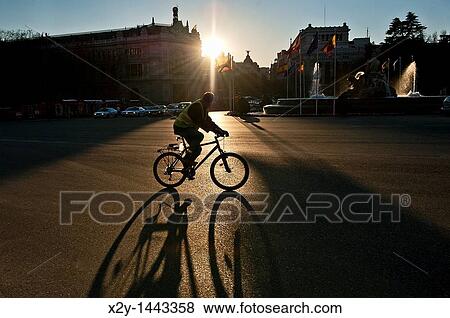 Stock Photo - Man riding a bike as the sun rises, Madrid, Spain. Fotosearch