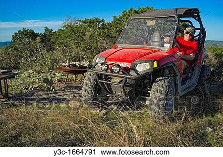 Stock Image - Man riding ATV Four Wheeler in rough terrain. Fotosearch