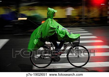 Stock Image - Man riding her bicycle in the rain, Hue, Central Vietnam, Vietnam. Fotosearch