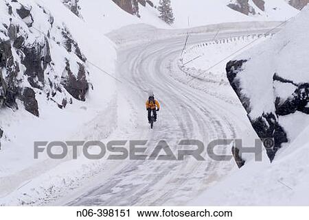 Stock Image - Man riding his mountain bike with a snowboard on his back in winter on Donner Summit, California. USA. Fotosearch