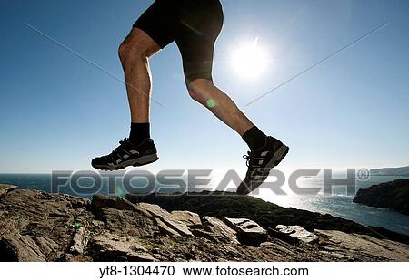 Stock Image - Man running along a rocky coastal path. Fotosearch