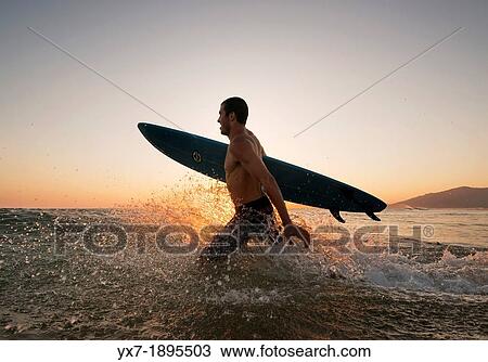 Stock Image - Man running into the sea with a surf board. Tarifa, Costa de la Luz, Cadiz, Andalusia, Spain, Europe.. Fotosearch