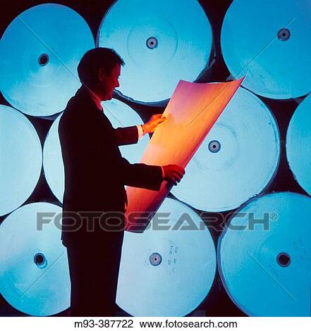 Stock Image - Man silhouetted in front of blue-lit industrial rolls of printing paper. Fotosearch