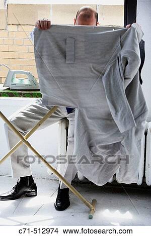 Man sitiing on radiator ironing clothes and hiding face with jacket View Large Photo Image Picture - Man sitiing on radiator ironing clothes and hiding face with jacket. Fotosearch