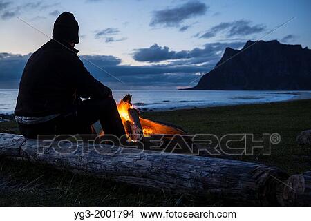 Man sits at evening campfire at Utakleiv beach, Lofoten Islands, Norway. View Large Photo Image Picture - Man sits at evening campfire at Utakleiv beach, Lofoten Islands, Norway.. Fotosearch