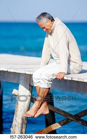 Man sitting down in a wooden footbridge over the sea View Large Photo Image Stock Photograph - Man sitting down in a wooden footbridge over the sea. Fotosearch