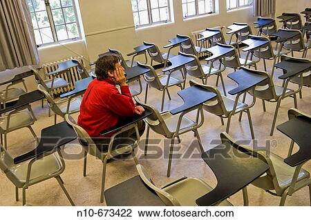 Stock Image - Man sitting in a student desk in an otherwise empty college classroom.. Fotosearch