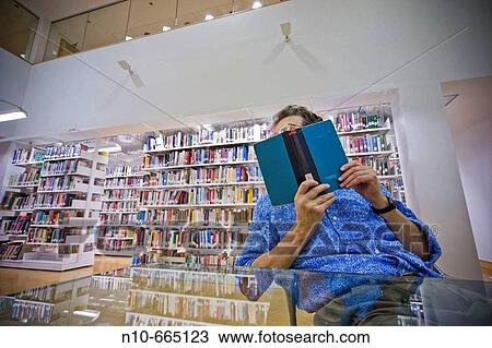 Man sitting in front of bookshelves at a library, reading a book. View Large Photo Image Stock Image - Man sitting in front of bookshelves at a library, reading a book.. Fotosearch