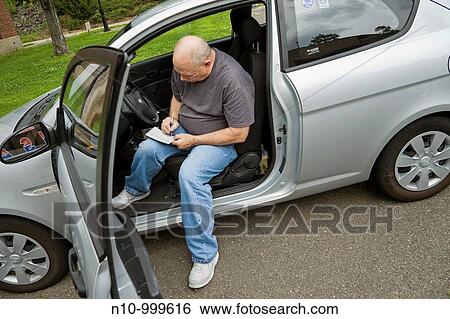Man sitting in his car, filling out a form View Large Photo Image Stock Photograph - Man sitting in his car, filling out a form. Fotosearch