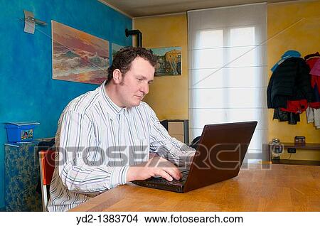 Man sitting in kitchen, using laptop View Large Photo Image Picture - Man sitting in kitchen, using laptop. Fotosearch