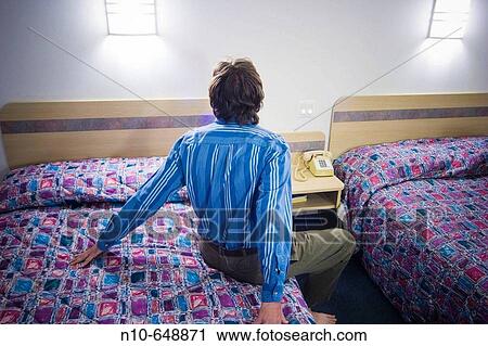 Man sitting on a bed in a hotel room. View Large Photo Image Stock Image - Man sitting on a bed in a hotel room.. Fotosearch
