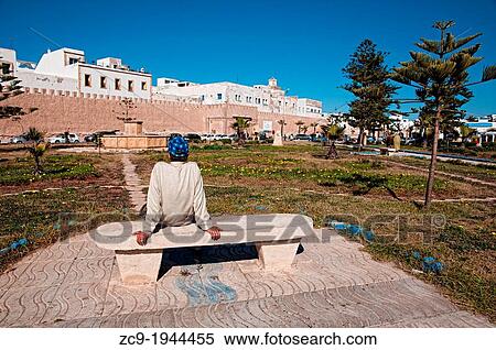 Man sitting on a bench of a park in front of Essaouira medina wall, Essaouira, Morocco. View Large Photo Image Stock Photography - Man sitting on a bench of a park in front of Essaouira medina wall, Essaouira, Morocco.. Fotosearch