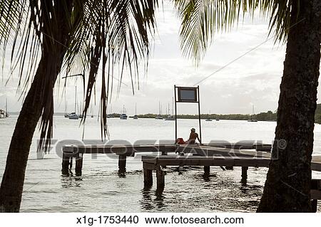 Man sitting on a dock looks towards the sea from Isla Colon, Bocas del Toro, Panama View Large Photo Image Stock Image - Man sitting on a dock looks towards the sea from Isla Colon, Bocas del Toro, Panama. Fotosearch