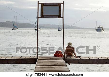 Man sitting on a dock looks towards the sea from Isla Colon, Bocas del Toro, Panama View Large Photo Image Stock Image - Man sitting on a dock looks towards the sea from Isla Colon, Bocas del Toro, Panama. Fotosearch