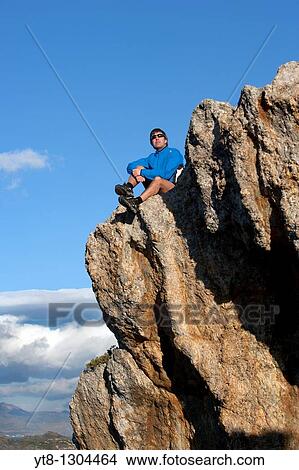 Man sitting on a rock ledge View Large Photo Image Picture - Man sitting on a rock ledge. Fotosearch