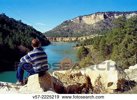 Man sitting on a rock, looking at the Jucar river. Serrania de Cuenca, Cuenca province, Castilla La Mancha, Spain. View Large Photo Image Stock Photo - Man sitting on a rock, looking at the Jucar river. Serrania de Cuenca, Cuenca province, Castilla La Mancha, Spain.. Fotosearch