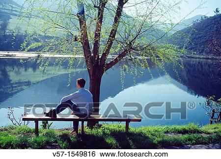 Man sitting on bench, looking at the lake. Cangas del Narcea, Asturias province, Spain. View Large Photo Image Stock Photograph - Man sitting on bench, looking at the lake. Cangas del Narcea, Asturias province, Spain.. Fotosearch
