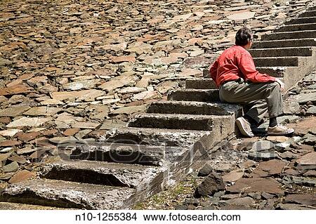 Picture - Man sitting on steps on a rock embankment. Fotosearch