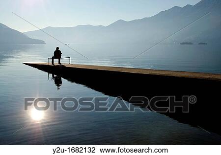 Man sitting on the pier close to the lake with mountains and islands View Large Photo Image Stock Image - Man sitting on the pier close to the lake with mountains and islands. Fotosearch