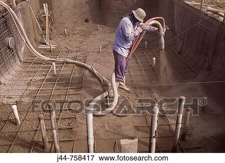Stock Photo - Man spraying concrete to bottom of pool under construction, Florida, USA. Fotosearch
