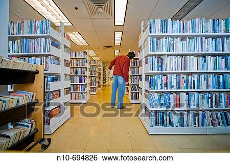 Man standing by bookshelves in a library View Large Photo Image Stock Photograph - Man standing by bookshelves in a library. Fotosearch