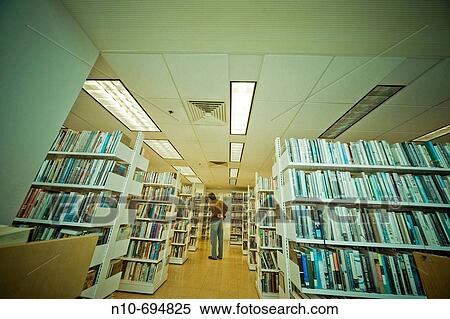 Man standing by bookshelves in a library View Large Photo Image Stock Photography - Man standing by bookshelves in a library. Fotosearch
