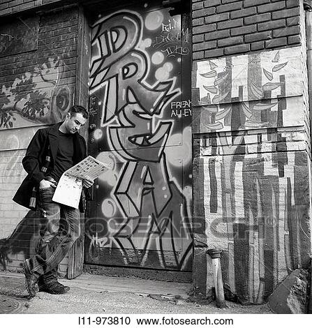 Stock Image - Man standing in alley reading newspaper.. Fotosearch