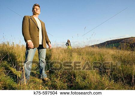 Picture - Man standing in field with woman in background. Fotosearch
