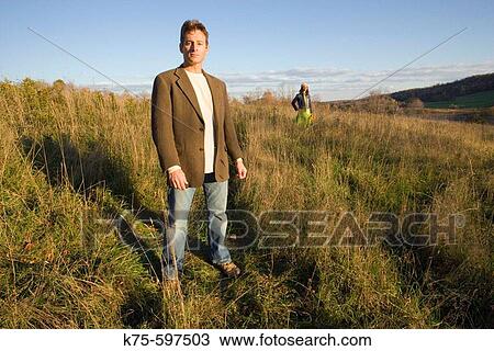 Man standing in field with woman in background View Large Photo Image Stock Image - Man standing in field with woman in background. Fotosearch