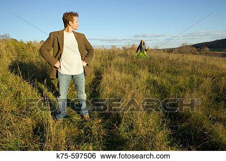 Man standing in field with woman in background View Large Photo Image Stock Photograph - Man standing in field with woman in background. Fotosearch