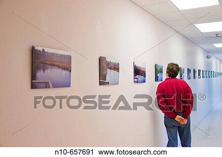Man standing in front of photographs hanging on a wall in an art gallery. View Large Photo Image Stock Image - Man standing in front of photographs hanging on a wall in an art gallery.. Fotosearch