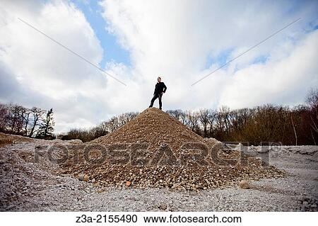 Man standing strong on a hill of stones. View Large Photo Image Stock Image - Man standing strong on a hill of stones.. Fotosearch