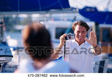 Stock Image - man taking a picture at the marina. Fotosearch