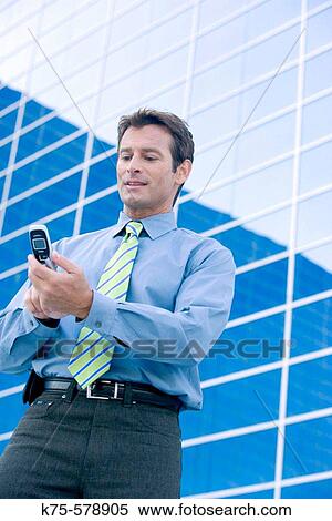 Stock Photography - Man text messaging on cell phone outside office building. Fotosearch