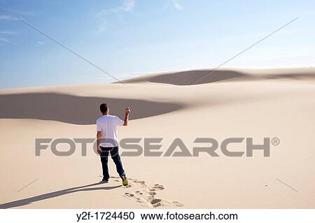 Stock Image - man trying to get mobile phone reception in dunes. Fotosearch