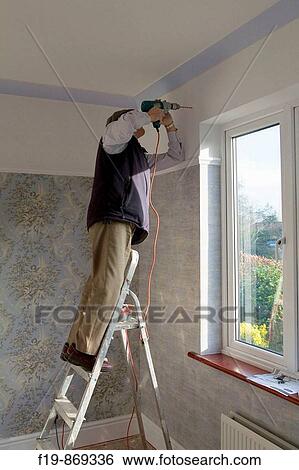 Stock Photograph - Man using an electric drill over window to put up curtain rail MR PR. Fotosearch