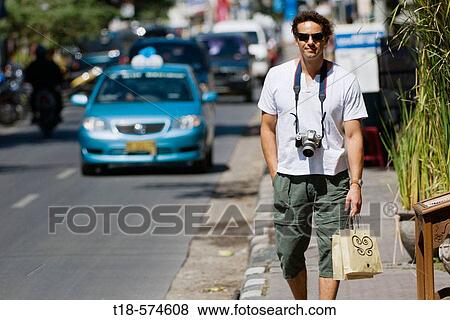 Stock Photo - man walking on sidewalk with busy traffic in the background. Fotosearch